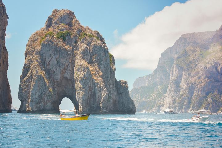 Capri – skała Faraglioni z łukiem, przez który przepływają łodzie